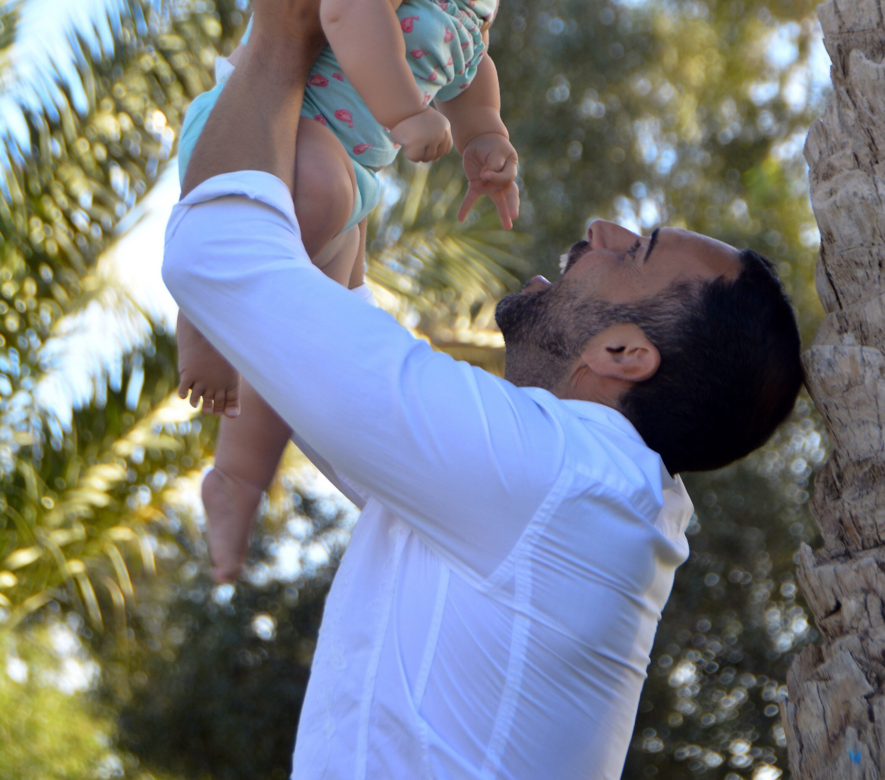 A father lifting his baby joyfully into the air beneath palm trees